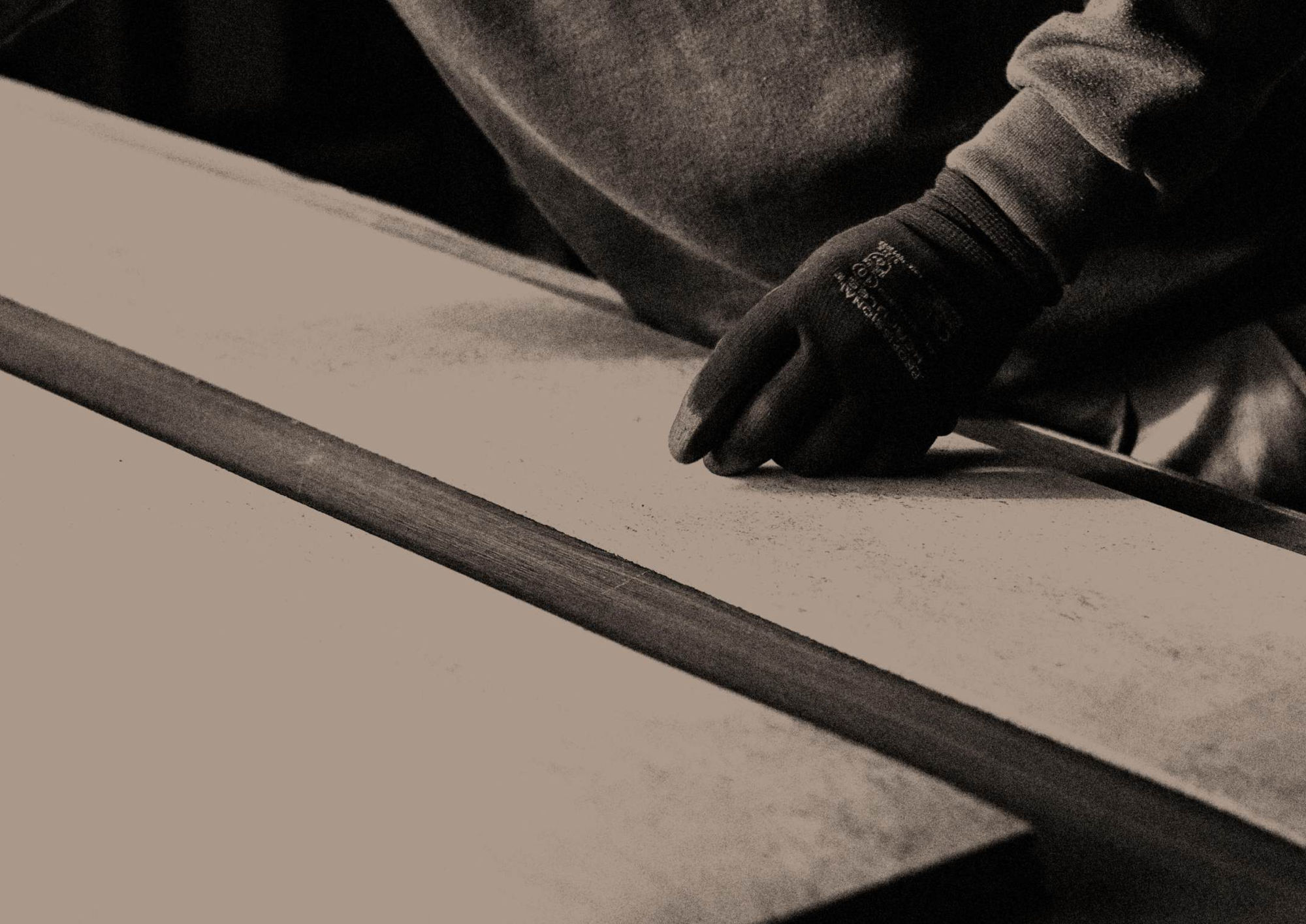 A craftsman's gloved hand guiding a cork panel